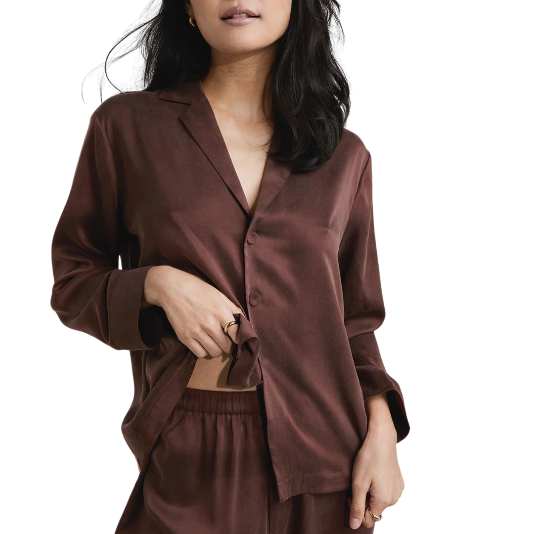 image of woman wearing the lunya washable silk pajamas in dozing umber holding up the shirt to see the elastic band 